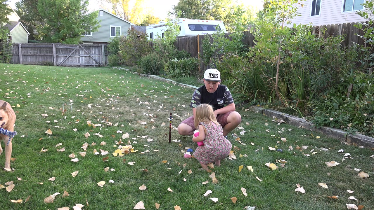 Father crouching with young child on backyard lawn as a dog enters frame.