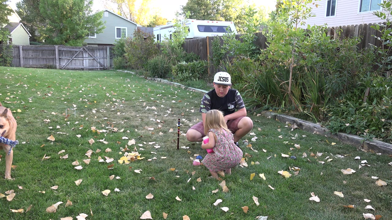 The child stands or squats close to the crouching father in the Westminster backyard as the dog appears along the right side of the frame.