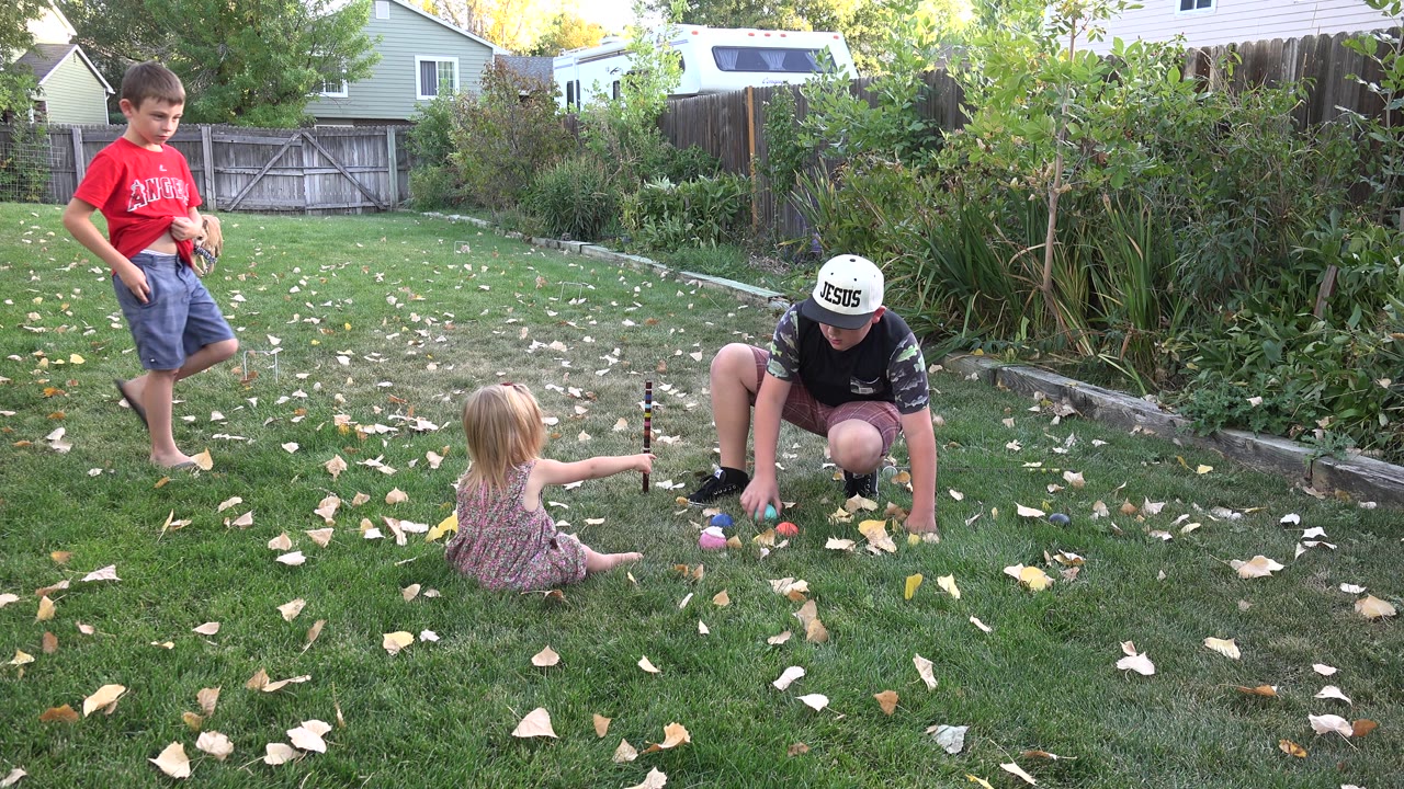 Children in a backyard with leaves on the grass and a dog in the background.