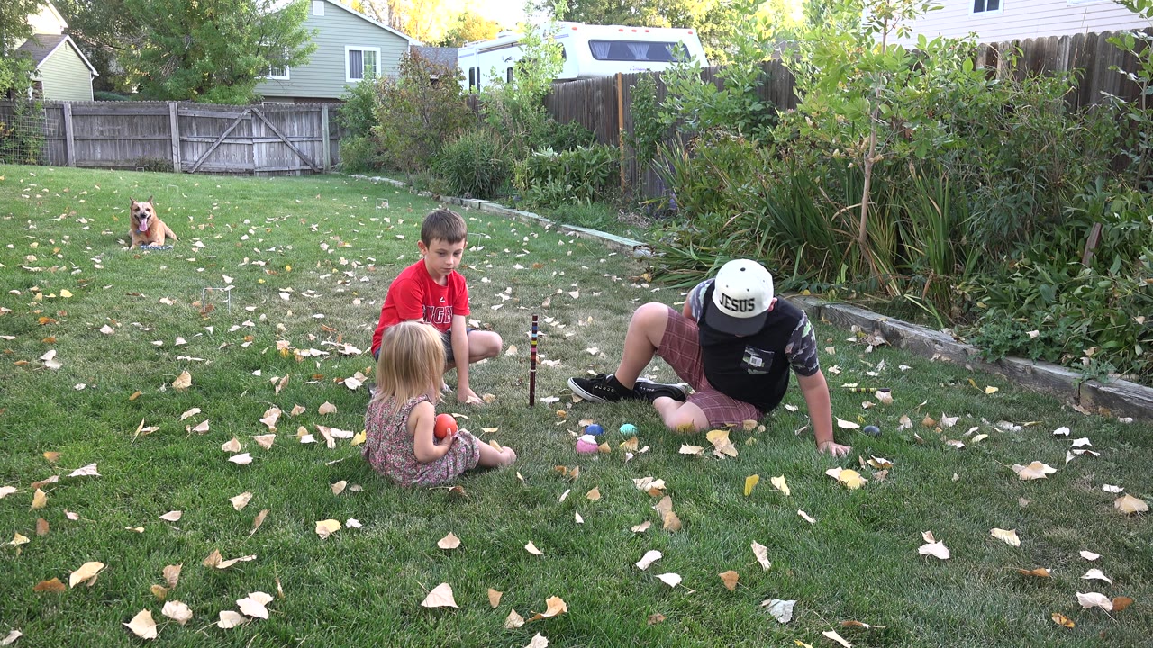 Children and an adult sitting on a backyard lawn with a dog in the background.