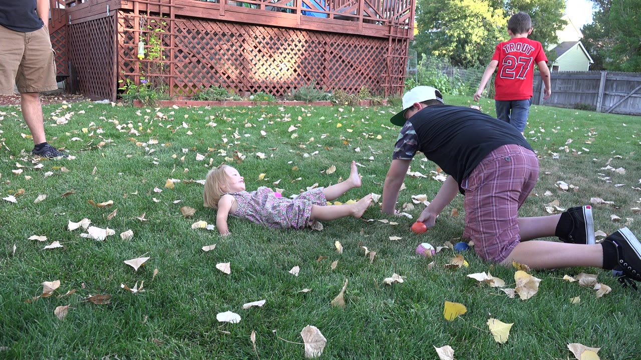 Children playing on backyard grass near a wooden deck.