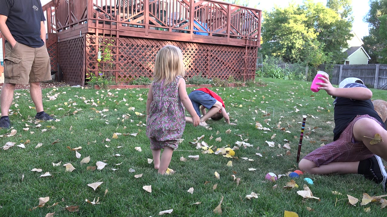 Boy in cap reaches across the lawn with a pink cup