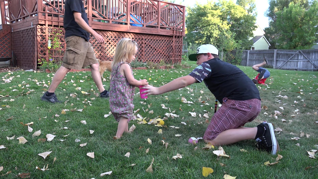 Small girl and kneeling boy on a lawn while another boy walks past.