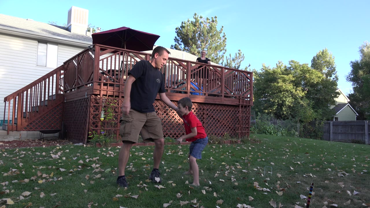Man and young boy playing in a backyard near a wooden deck.
