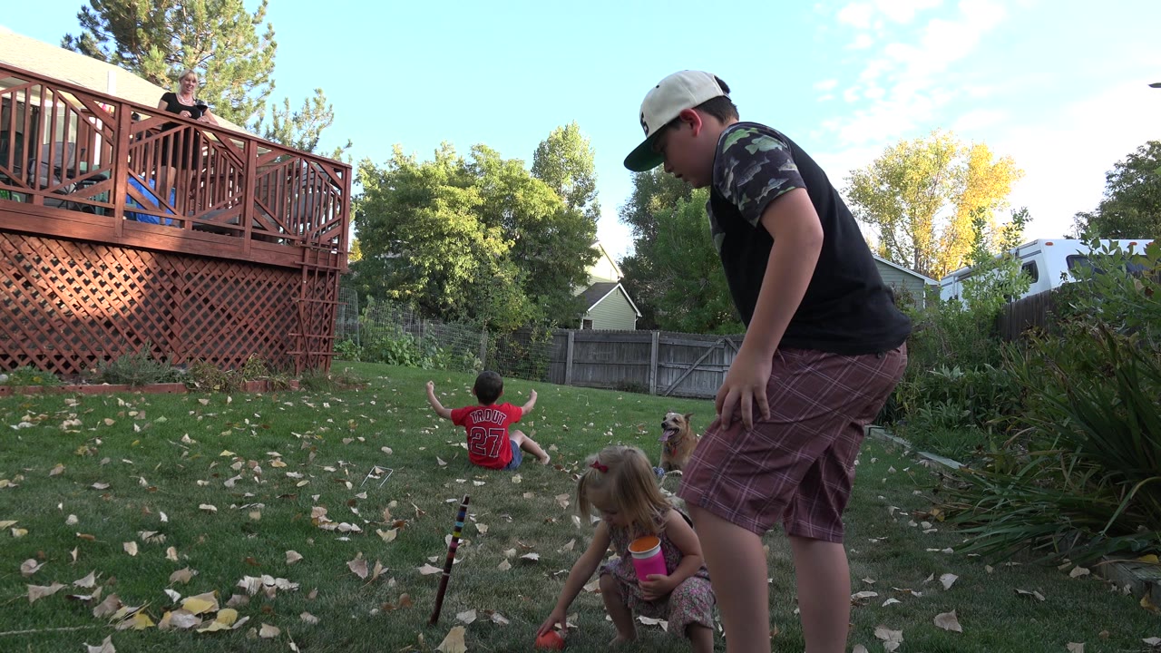 Adults, children, and a dog in a sunny backyard near a wooden deck.