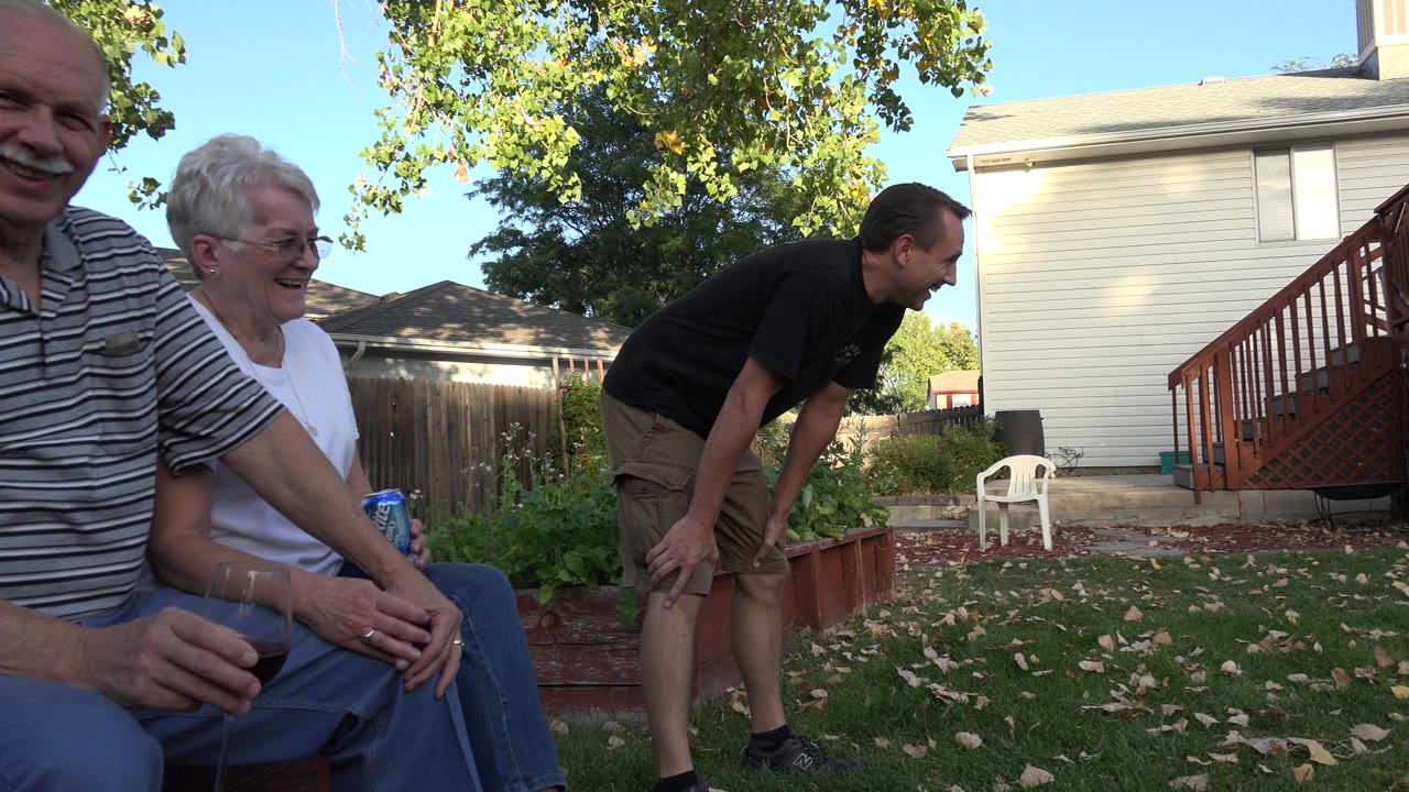 Older couple seated in foreground with younger man leaning in background.