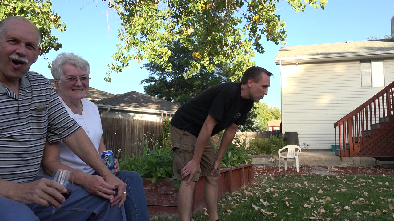 Adults seated near a backyard garden with a man standing nearby.