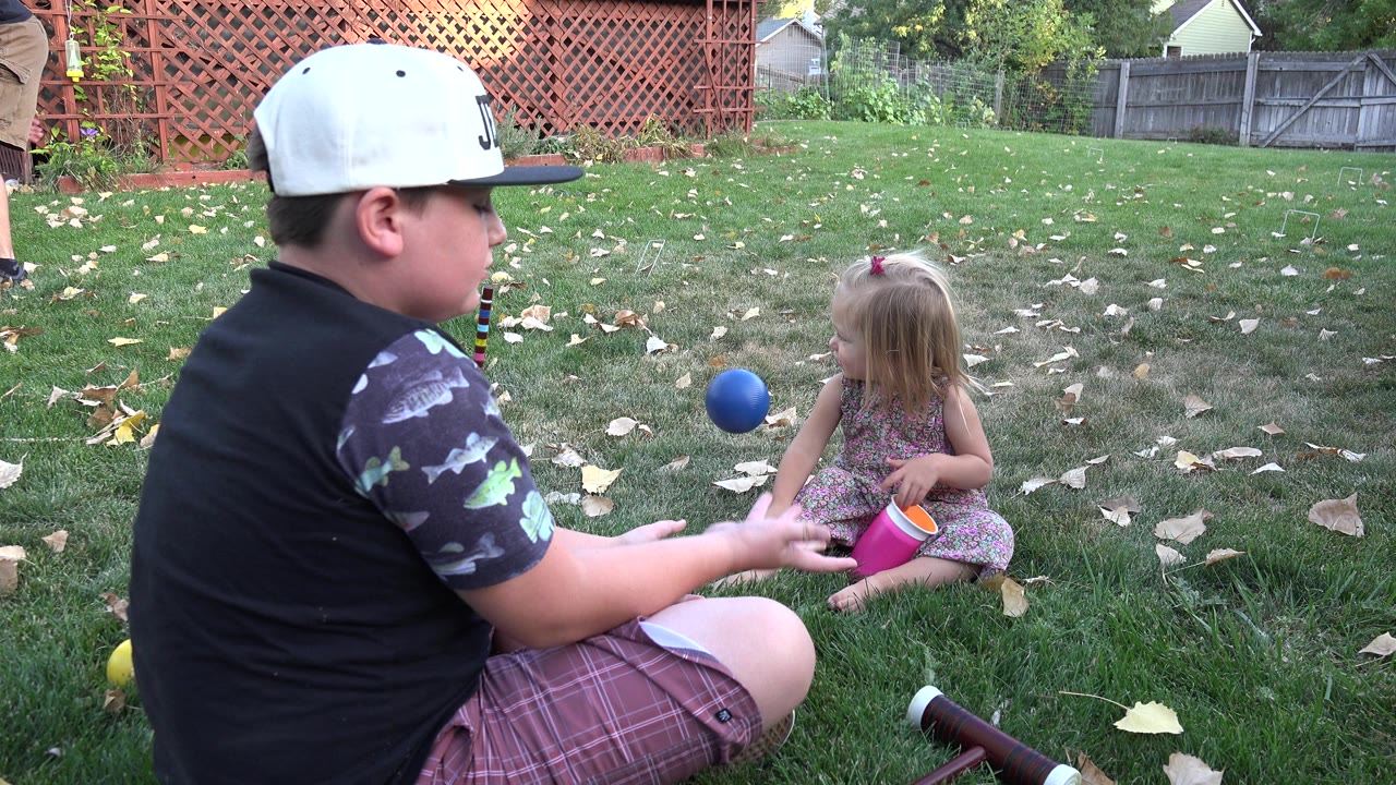 In Westminster, Colorado, the seated boy reaches toward a blue ball between him and the little girl, while a pink-and-orange cup rests near her on the lawn.