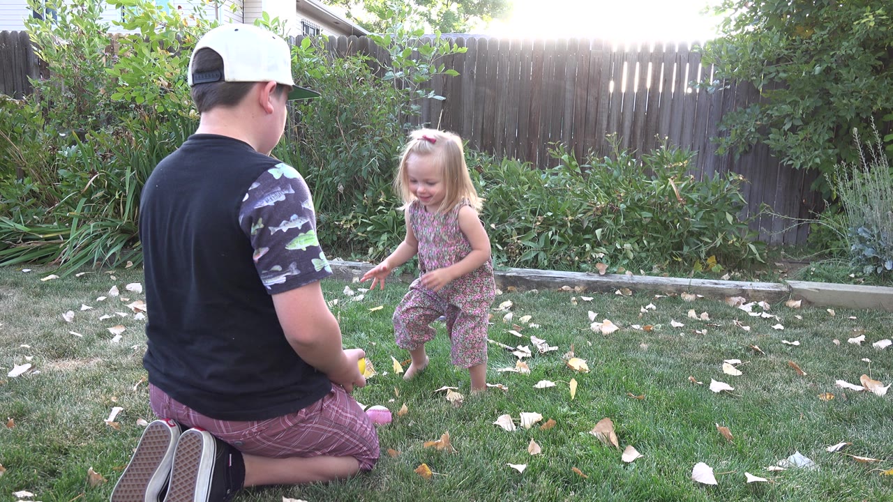 Man kneeling on grass near a young girl in a backyard.