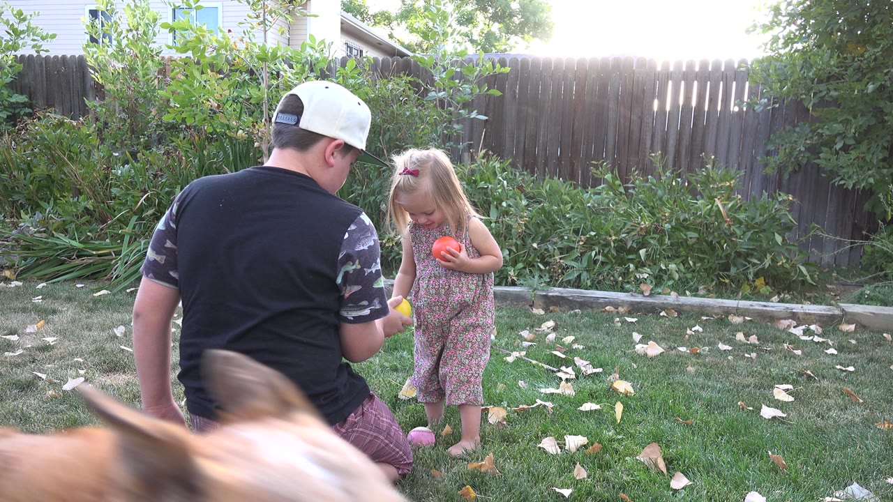 Boy kneeling near young girl holding balls in a backyard.