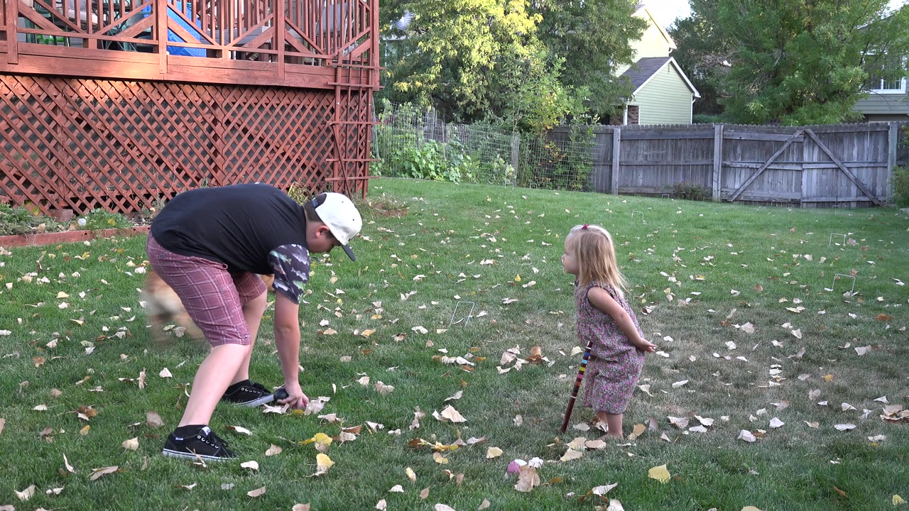 Man bending on a backyard lawn near a young child.