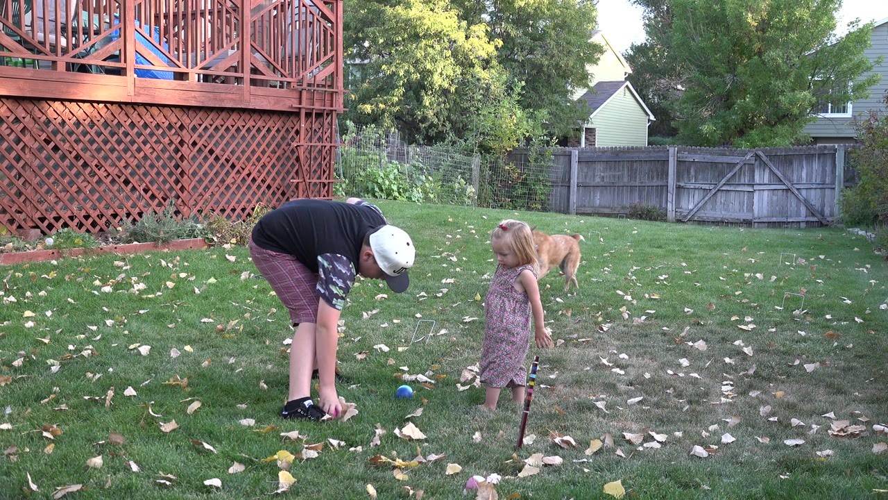 Boy bends near a ball while a girl stands in a backyard with a dog behind her.
