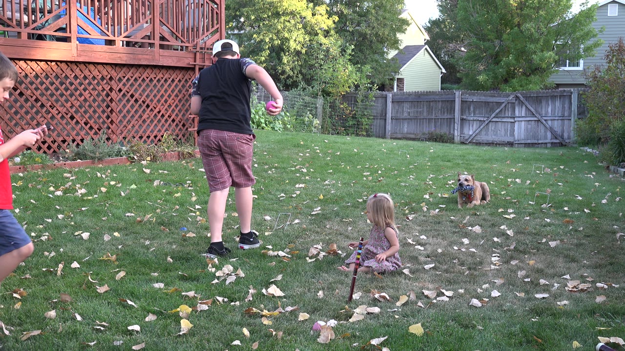 Adult and children in a backyard with a small dog near the fence.