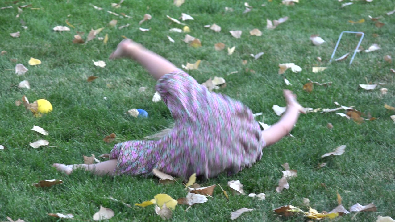The girl is partly turned away while rolling on the Westminster lawn, with dry leaves scattered around her and a yellow ball in the background.
