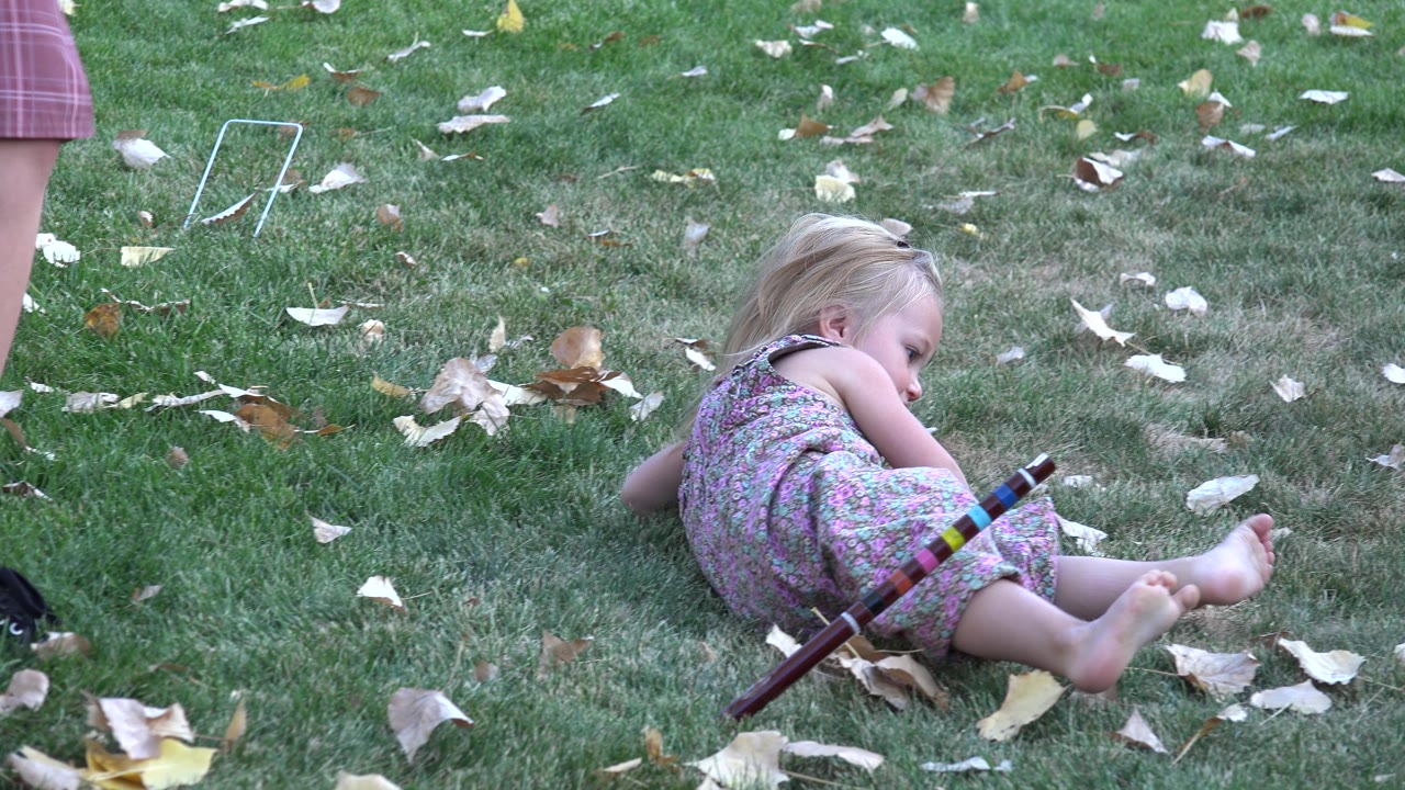 Girl curled on the grass beside dry leaves and a striped toy.