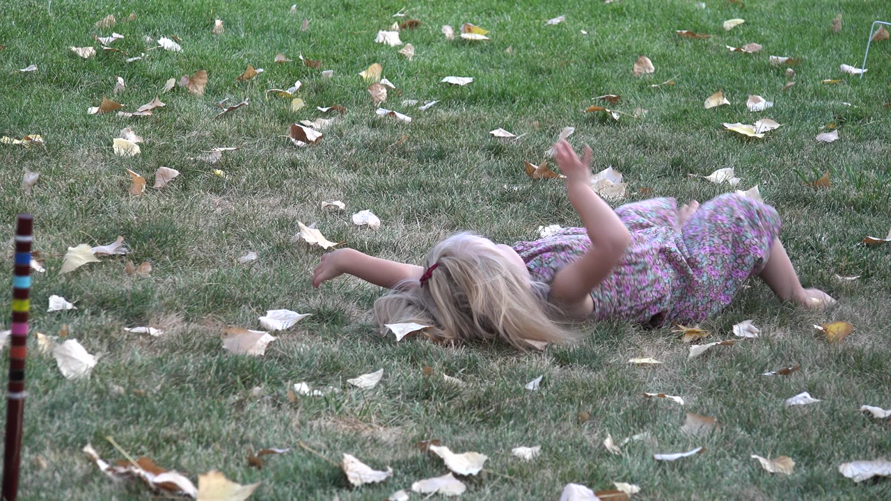Young blonde girl in a floral dress lies face down on grass with scattered leaves in Westminster, Colorado.