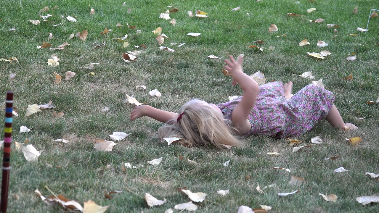 Young girl in a floral dress remains low on the grass in Westminster, Colorado, with one arm lifted and leaves spread around her.