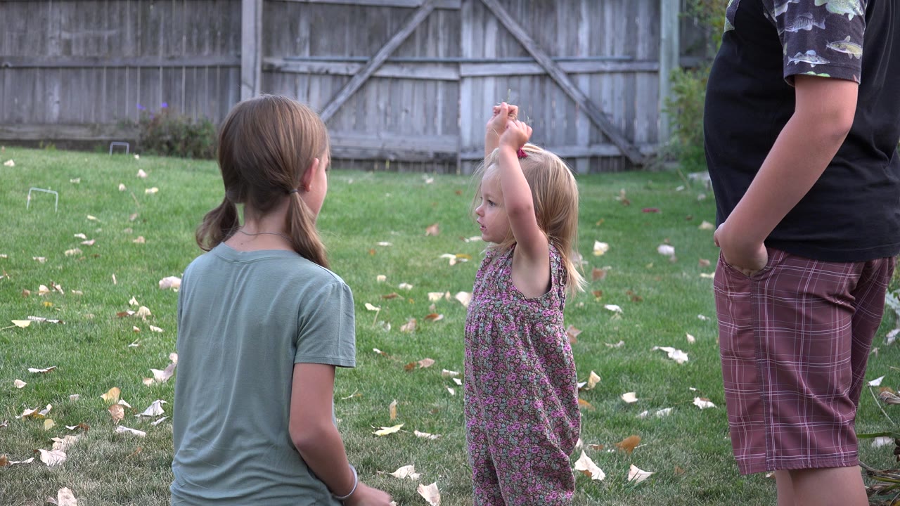 Two girls and a cropped adult stand on a backyard lawn.