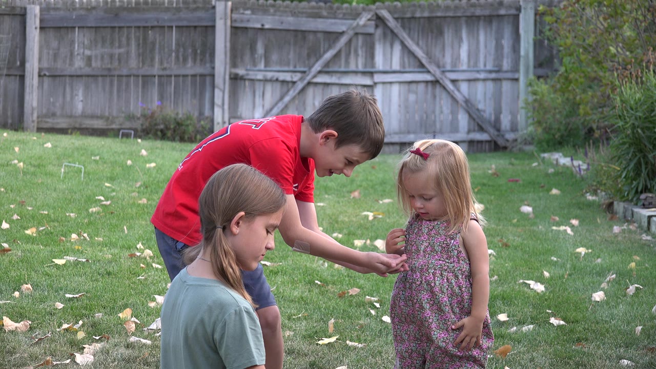 In Westminster, Colorado, a boy in a red shirt leans toward a small blonde girl while another child sits in the foreground on the grass.