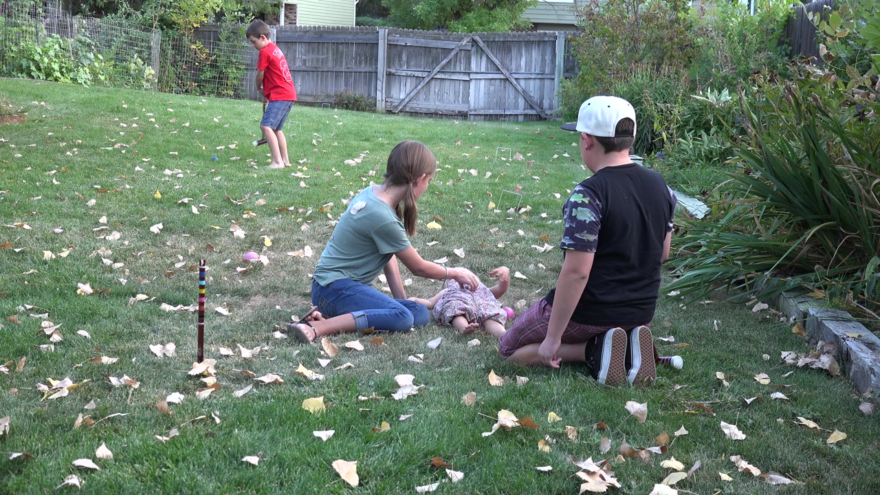Children on a backyard lawn with one child standing and others seated nearby.
