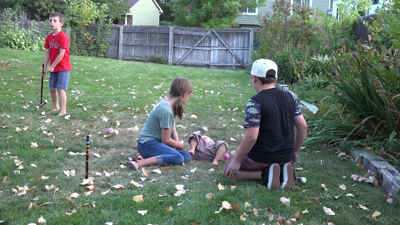Children and adults on a backyard lawn during a game.