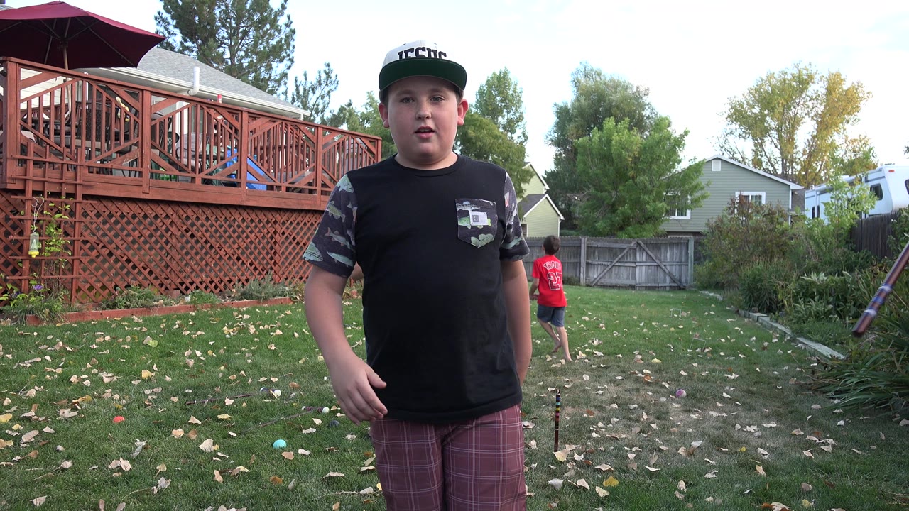 Young boy standing on a leaf-strewn backyard lawn near a red deck.
