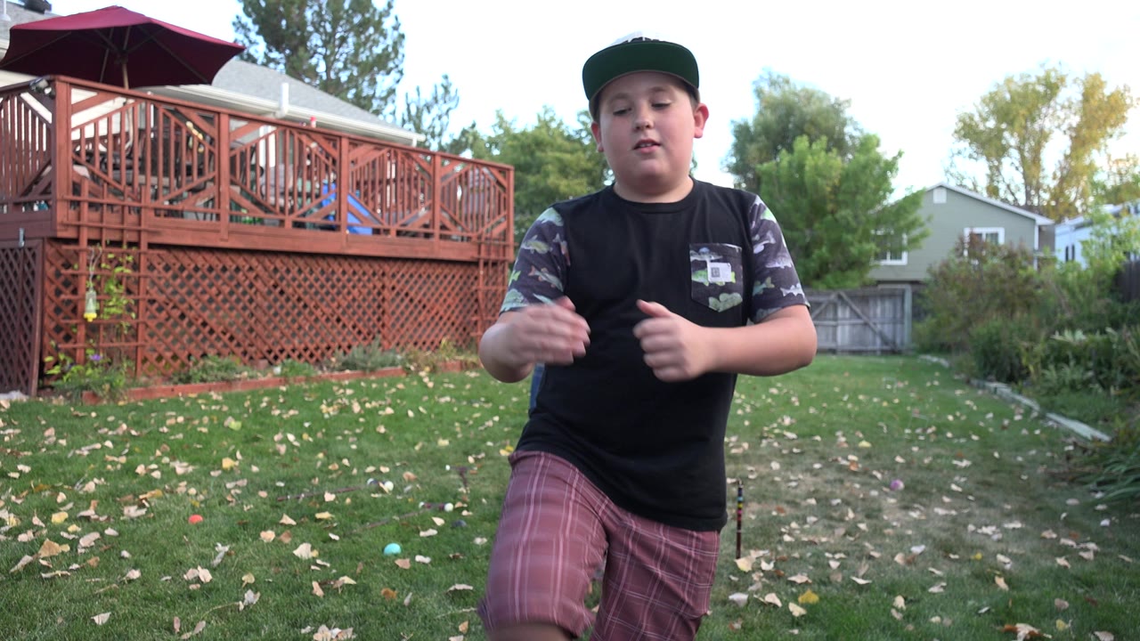 Boy in a baseball cap standing in a backyard near a red deck.