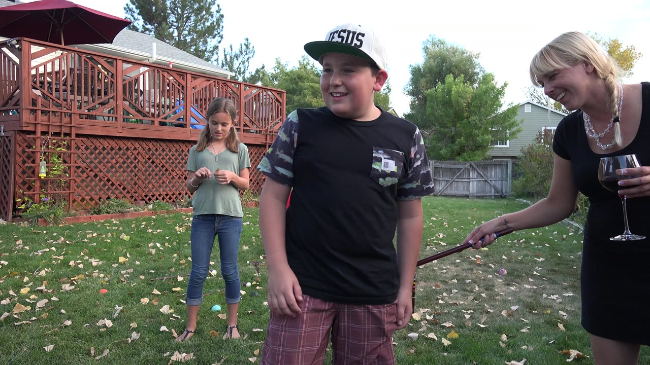 In Westminster, Colorado, the boy faces slightly left beside croquet equipment while the girl stands farther back on the lawn and the woman with a wine glass remains at the right edge.
