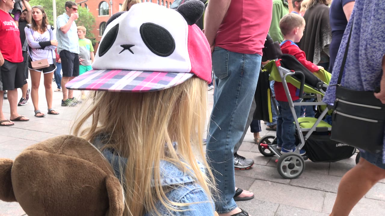 Close profile of child wearing a pink panda cap in a crowded plaza.