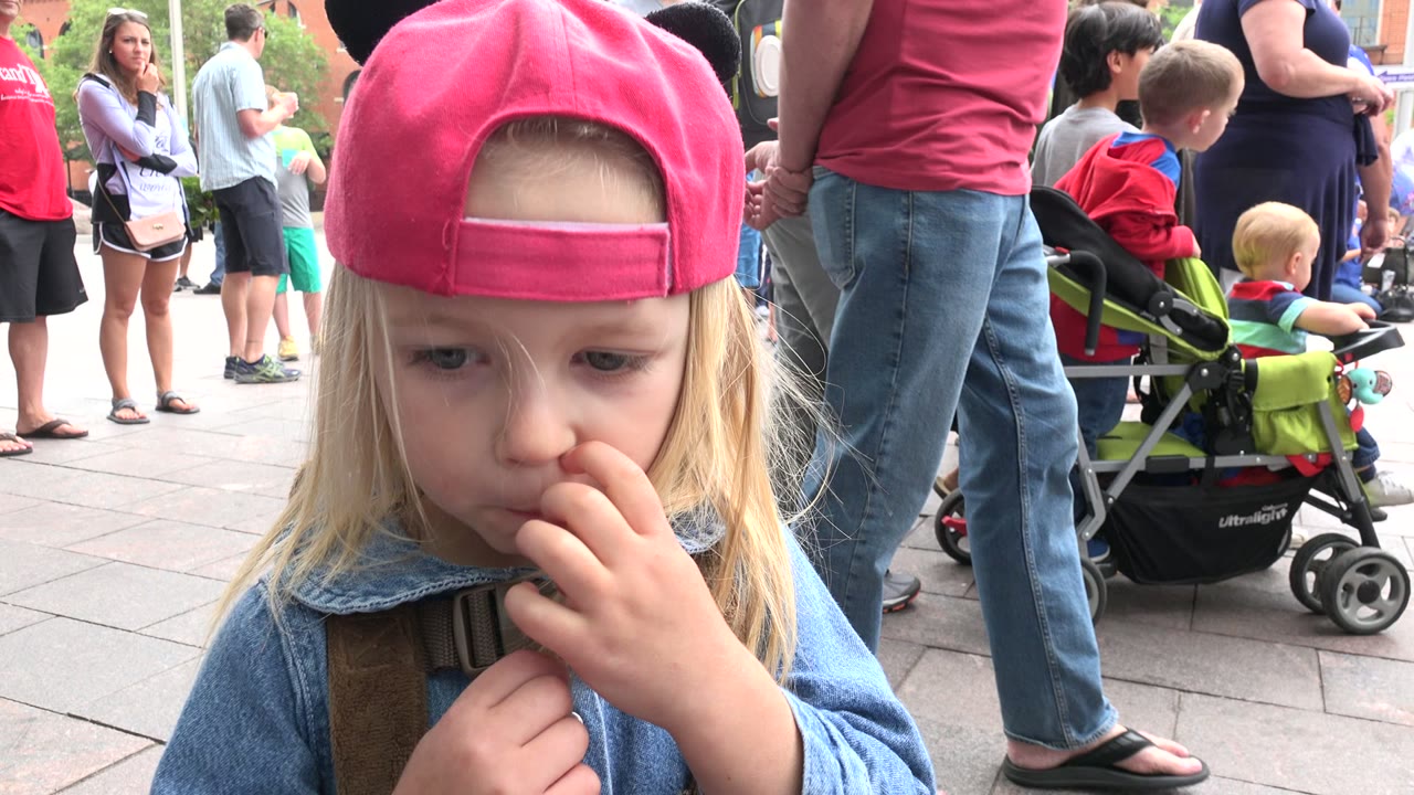 The child faces forward with a hand near their mouth while adults, children, and a stroller stand behind in Grand Junction, Colorado.