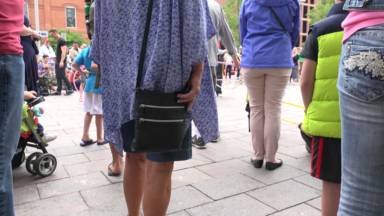 At the start of the Grand Junction, Colorado clip, the camera looks across paving stones toward standing adults, a child, a stroller, and the edge of a tan dog near the lower frame.