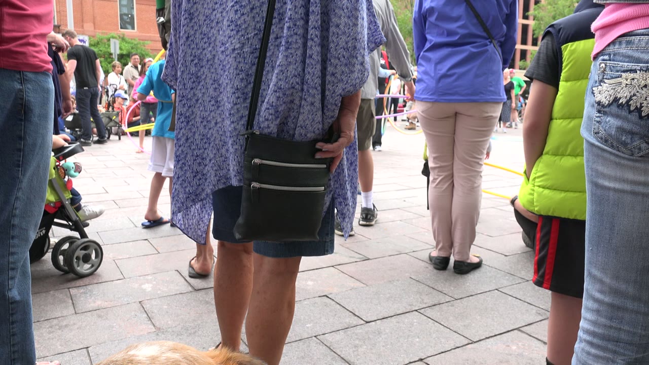 One second into the Grand Junction, Colorado footage, the low camera frames adult legs, a stroller, a child in a bright vest, and a small portion of the tan dog at the bottom.