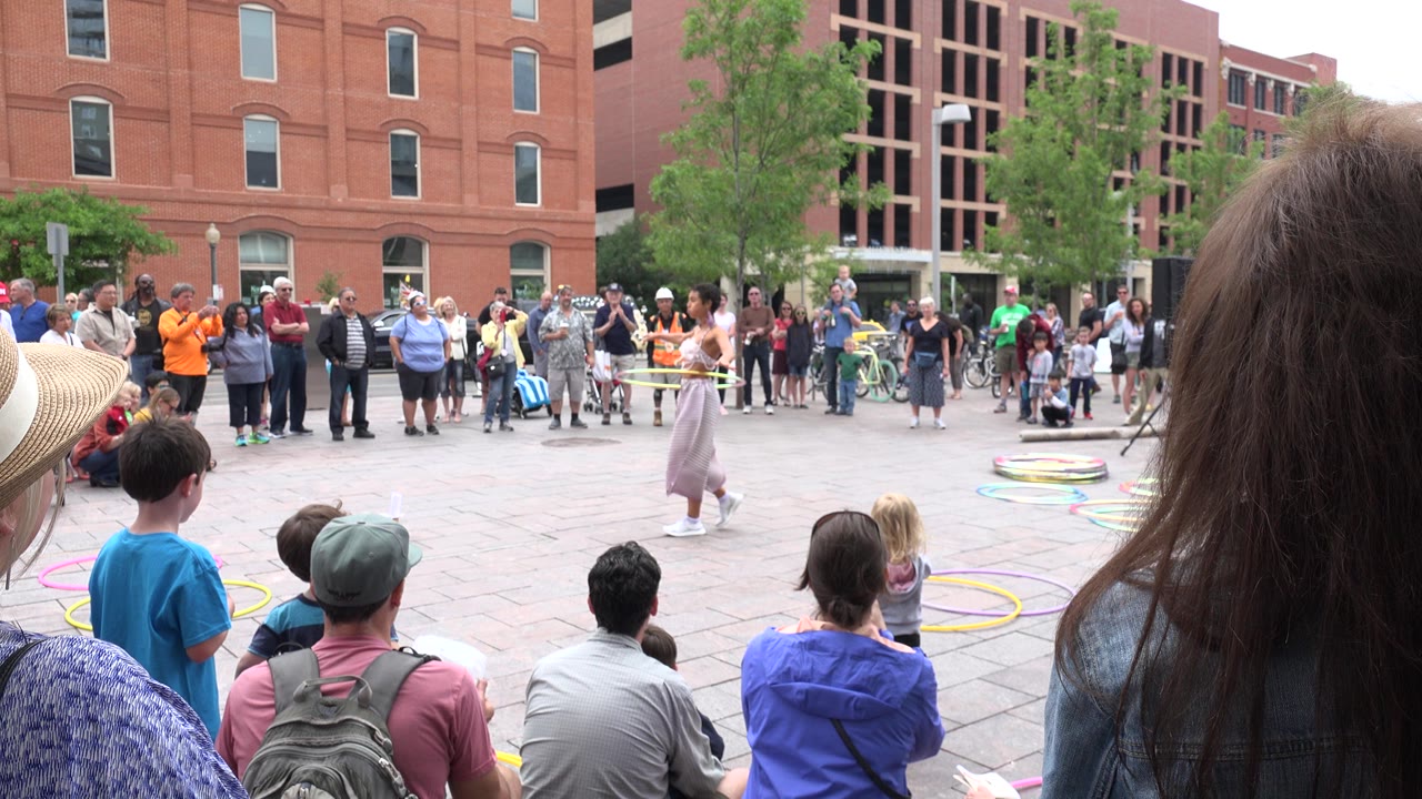 Crowd watches a woman hula hoop in a plaza.