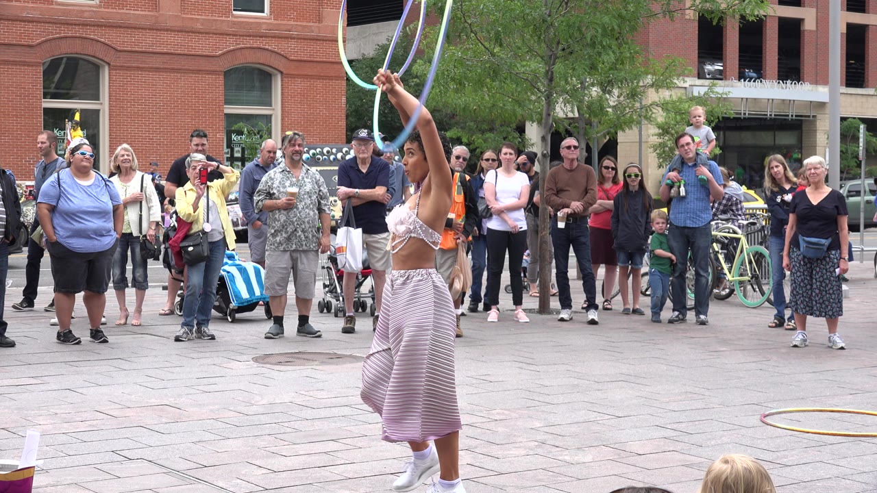 Hula hoop performer lifting hoops before a street crowd.