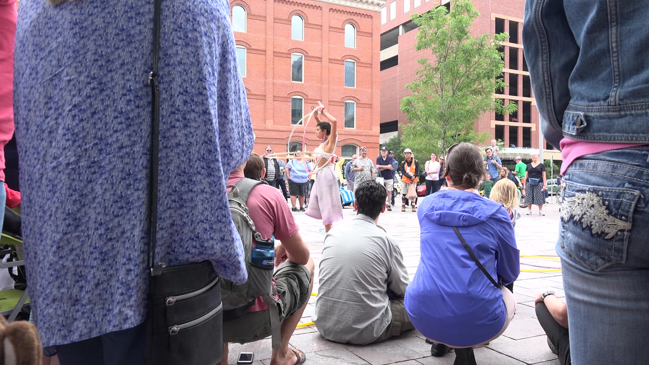 Audience watches a woman performing with hoops in a public square.