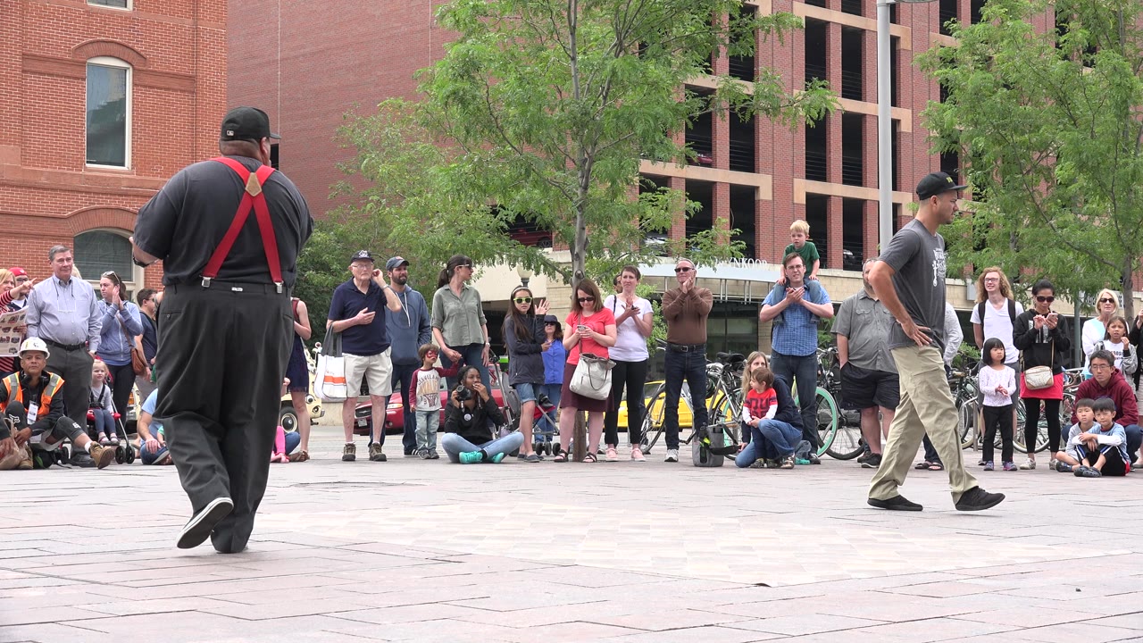 The two street performers hold positions several steps apart as spectators stand and sit behind them in Grand Junction, Colorado.