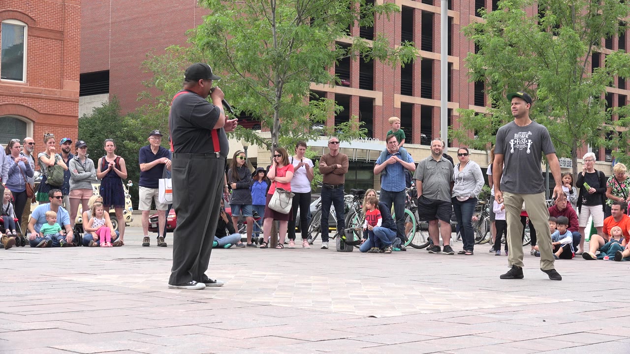 Two street performers stand before a crowd in a paved plaza.