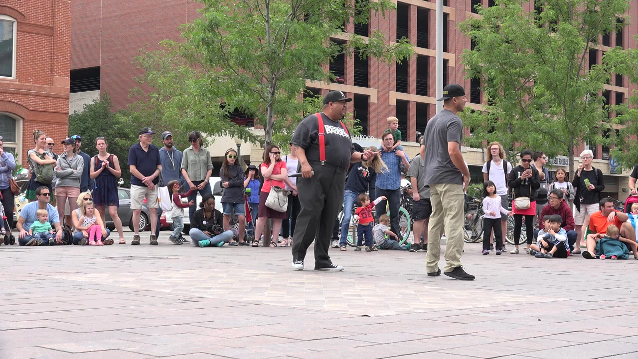 Two street performers face each other before a crowd in a plaza.