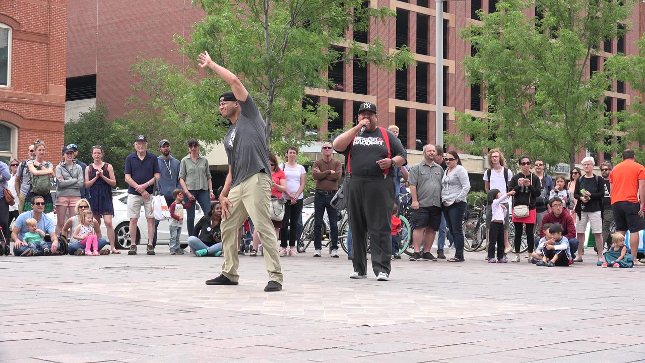 Street performer gestures in front of a crowd on a paved plaza.