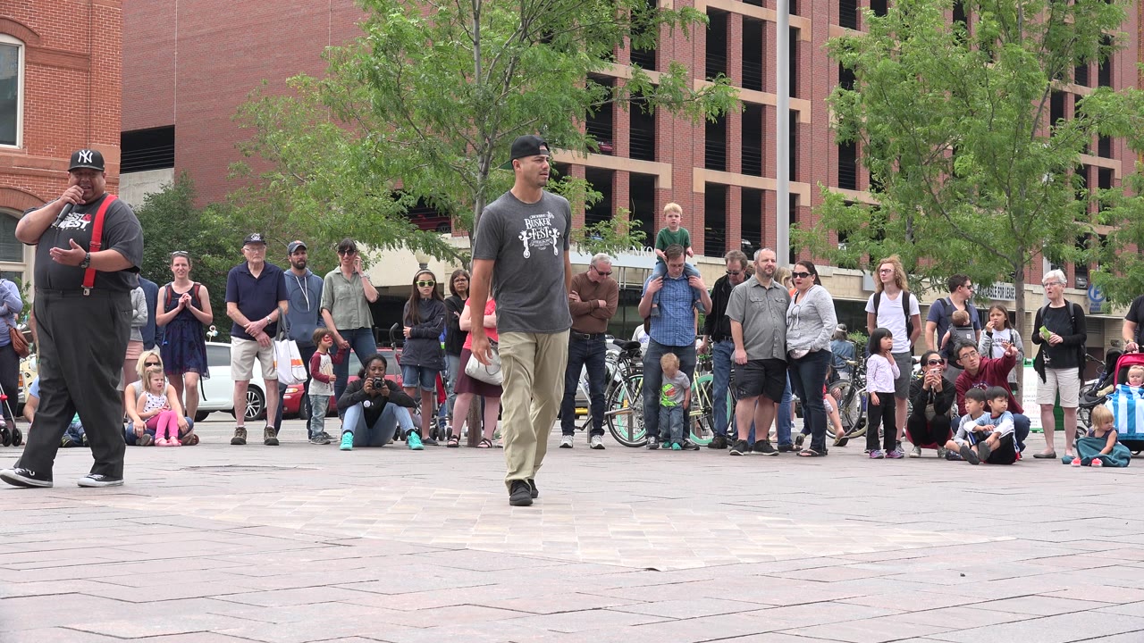 The performer stands nearer the center of the frame in Grand Junction, Colorado, with seated children and standing adults watching from the plaza edge.