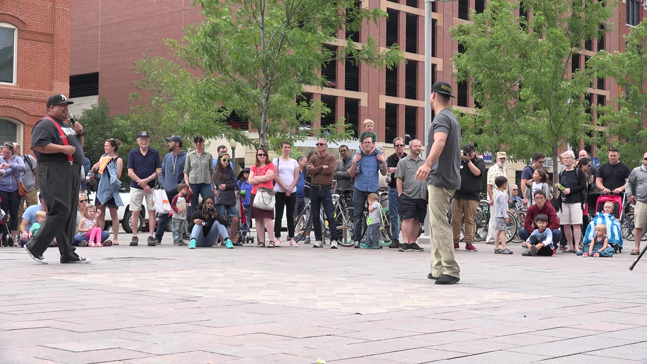 Two street performers stand before a crowd in a paved plaza.