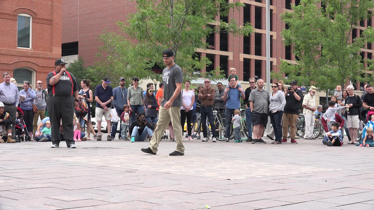 Two street performers stand before a crowd in a paved plaza.