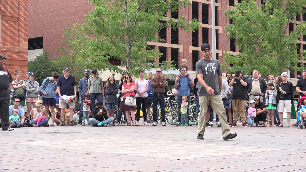 Street performer walks across an open plaza in front of a watching crowd.