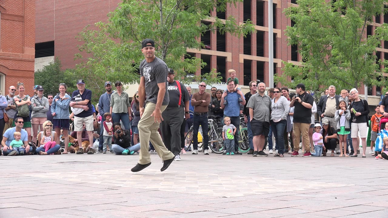 Street dancer stepping across a plaza in front of a crowd.