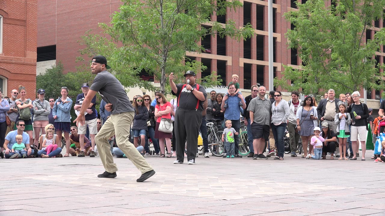 Man dancing in front of a large crowd on a paved plaza.