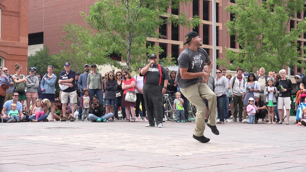 Man in gray shirt dances in front of an outdoor crowd.