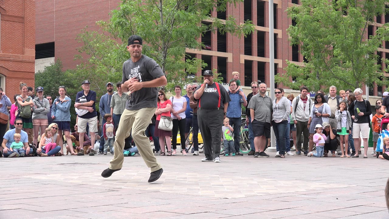 Break dancer stepping on a paved sidewalk in front of a watching crowd.