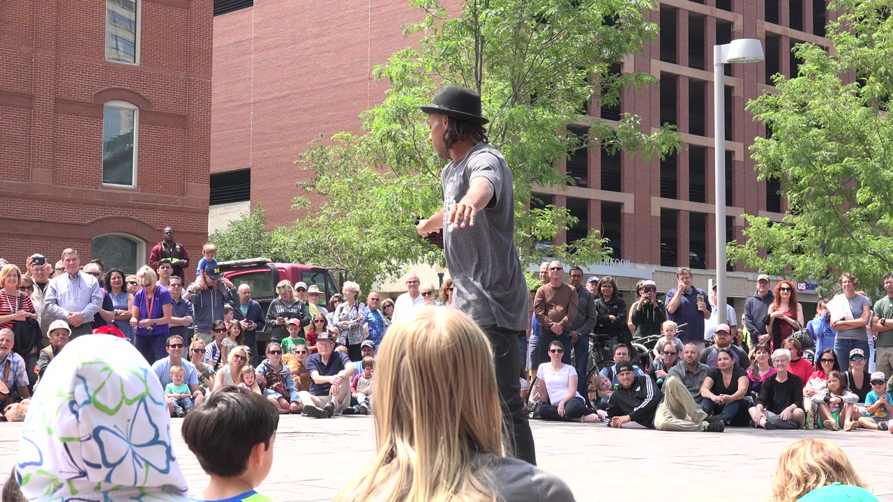 Street performer facing a seated crowd in a public plaza.