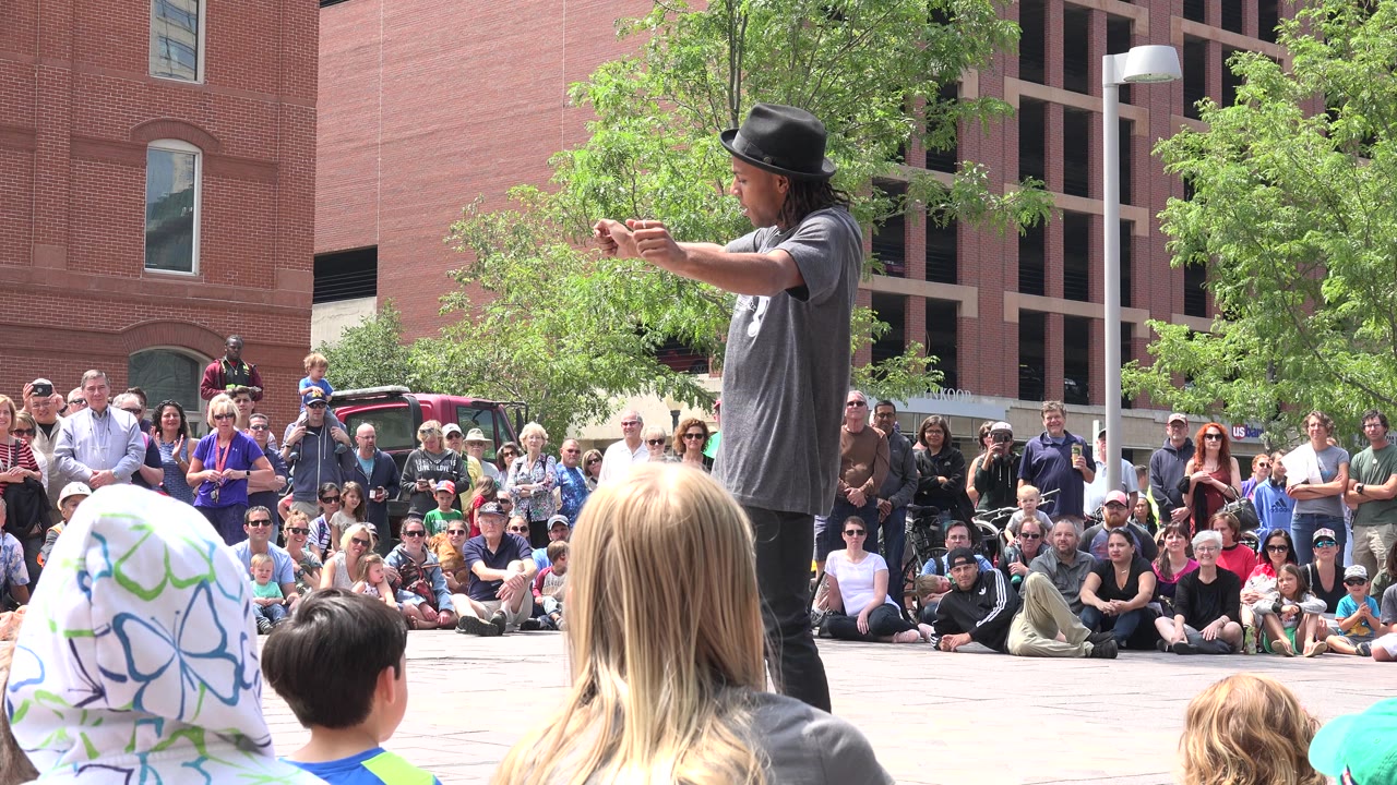 Street performer gesturing toward a seated plaza crowd.
