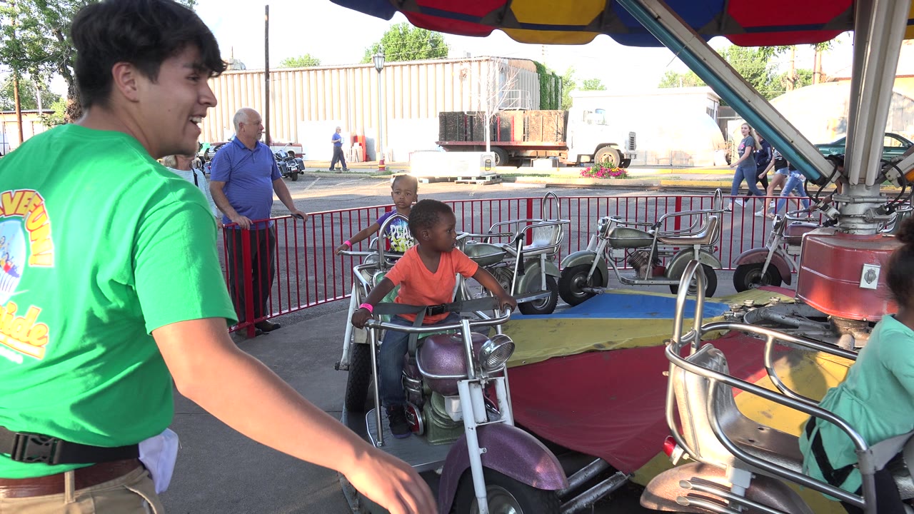 Green-shirted operator gestures beside children riding under a canopy.